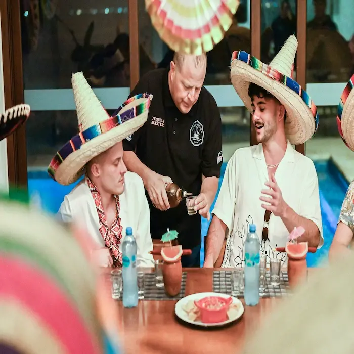Male Tequila Master pouring tequila for two guests wearing sombreros during a fun tasting experience in Cancun.